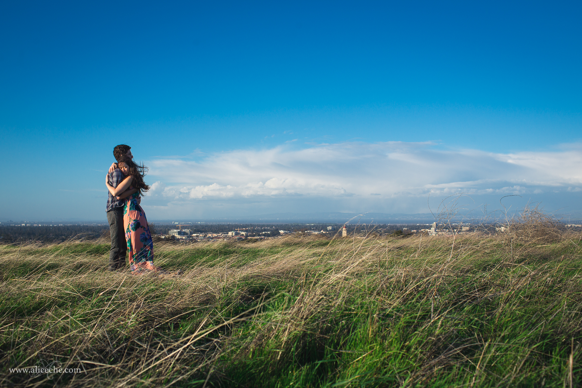 alice-che-photography-stanford-windswept-couple-hugging-blue-skies-green-grass