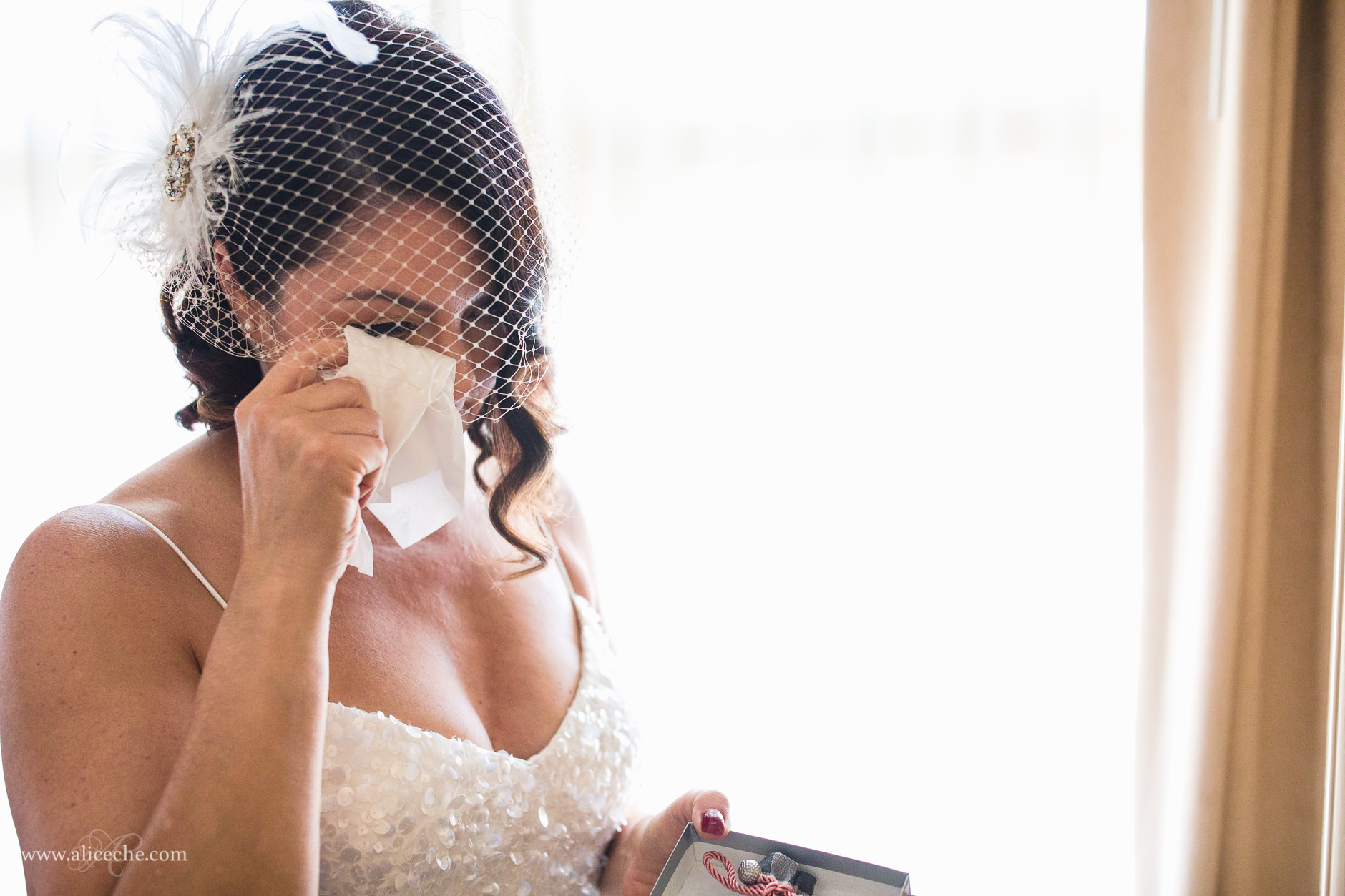 Backlit photo of bride with fascinator wiping away a tear