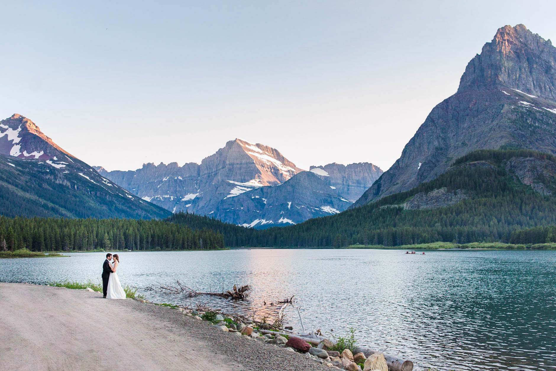 Many Glacier Park destination wedding bride and groom by lake surrounded by snow capped mountains