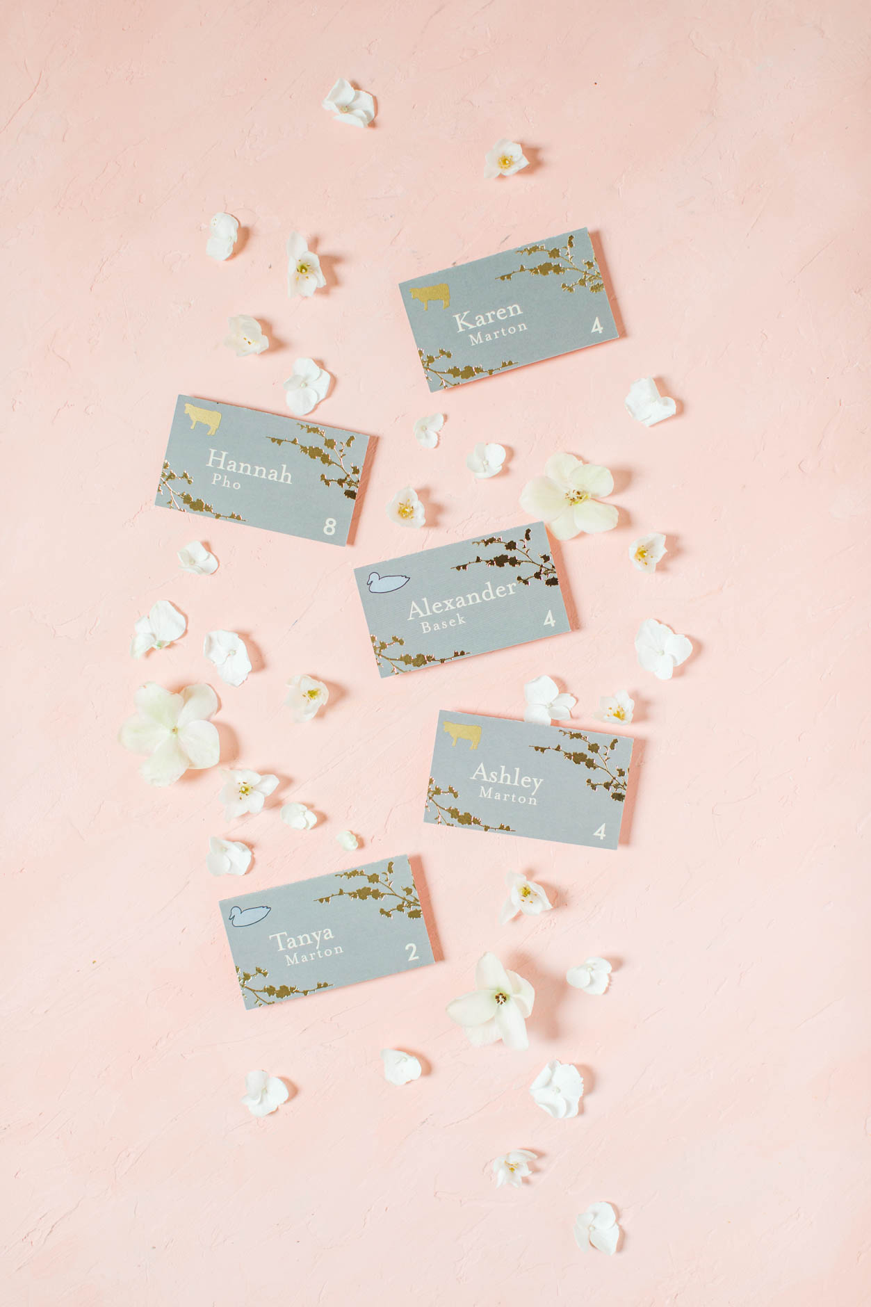 Five gray and gold escort cards surrounded by hydrangea florets in a wedding flat lay