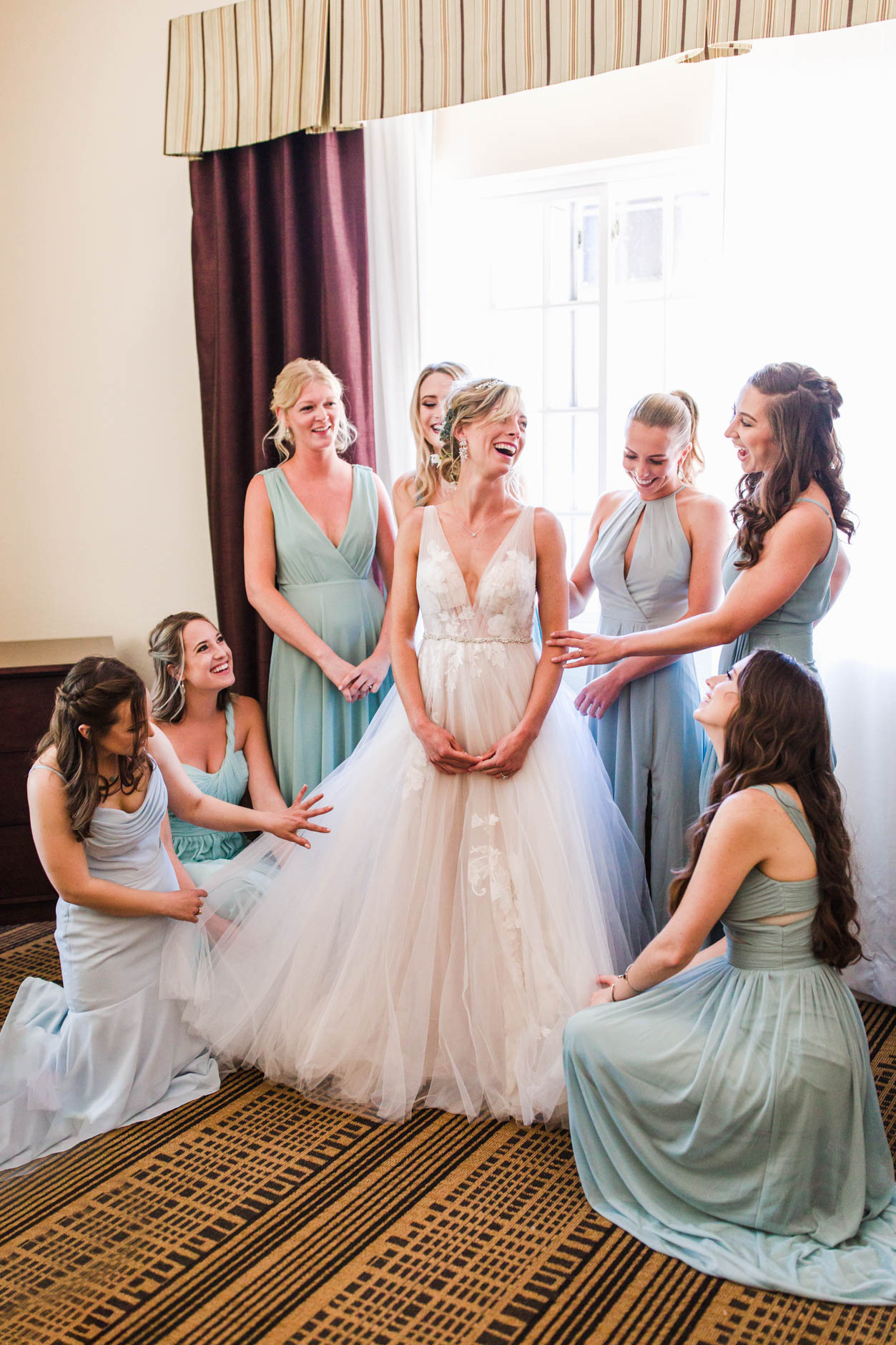Bride laughing with her bridesmaids who are helping her get ready
