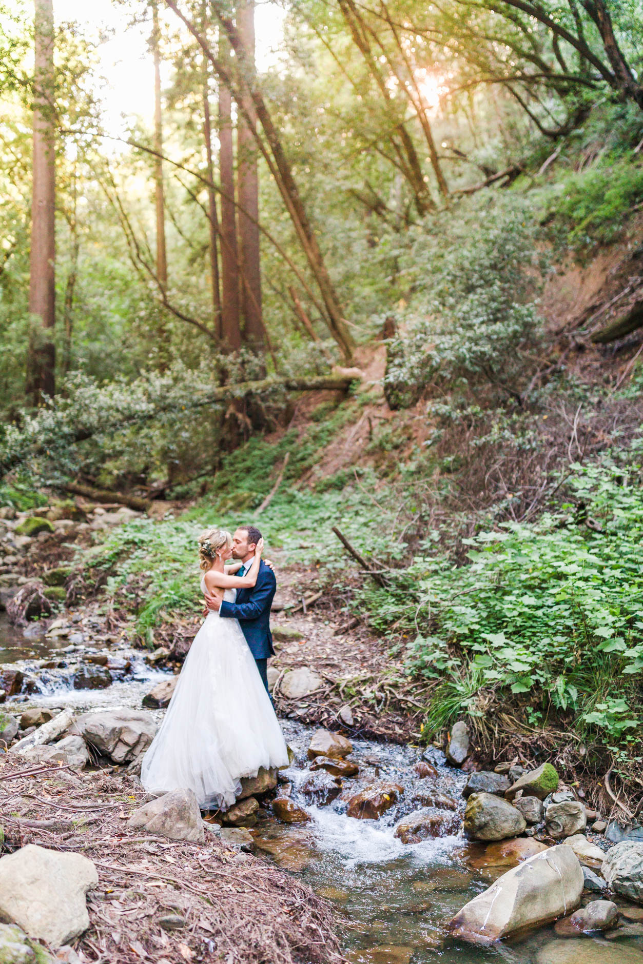 Bride and Groom kissing in creek among the redwoods with sun pouring in