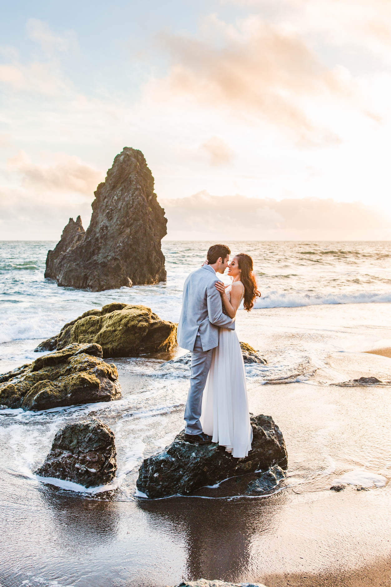 Bride and Groom standing on rock on beach at sunset