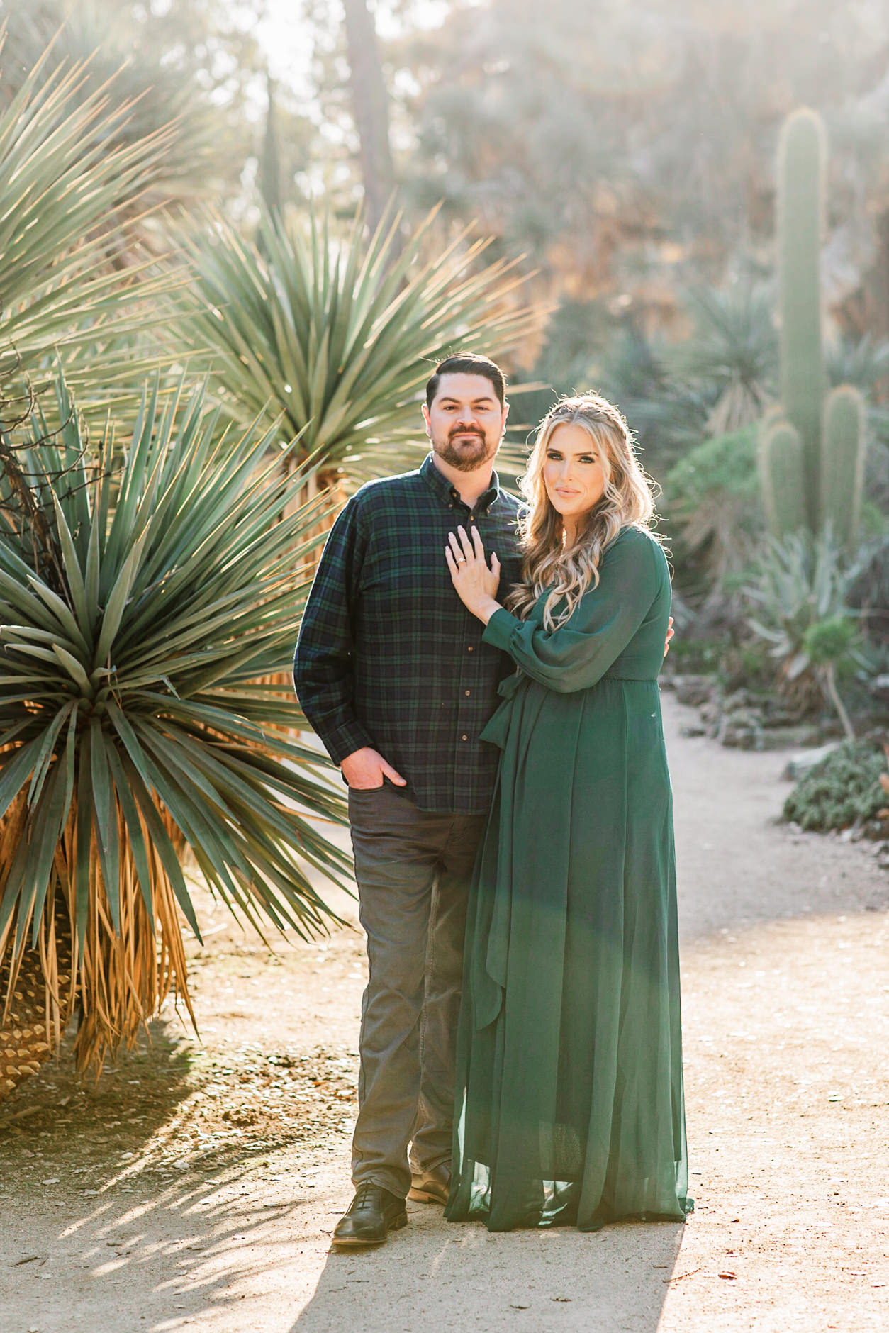 Woman in green maxi dress with her hand on her fiance's chest standing in front of the cacti at the Arizona Cactus Garden on Stanford Campus
