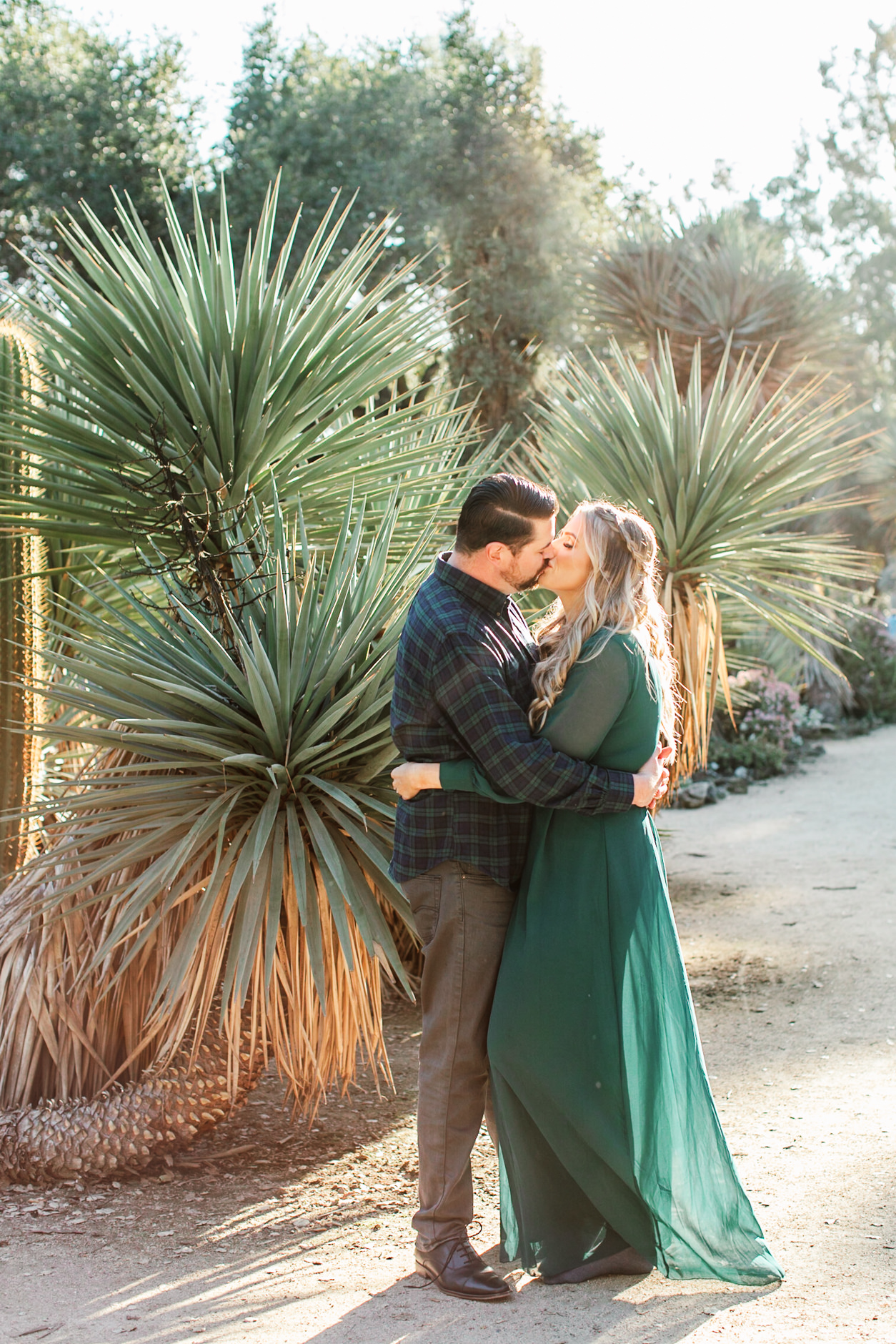 Woman in flowy green dress kissing her fiance in the Arizona Cactus Garden during their Palo Alto engagement session