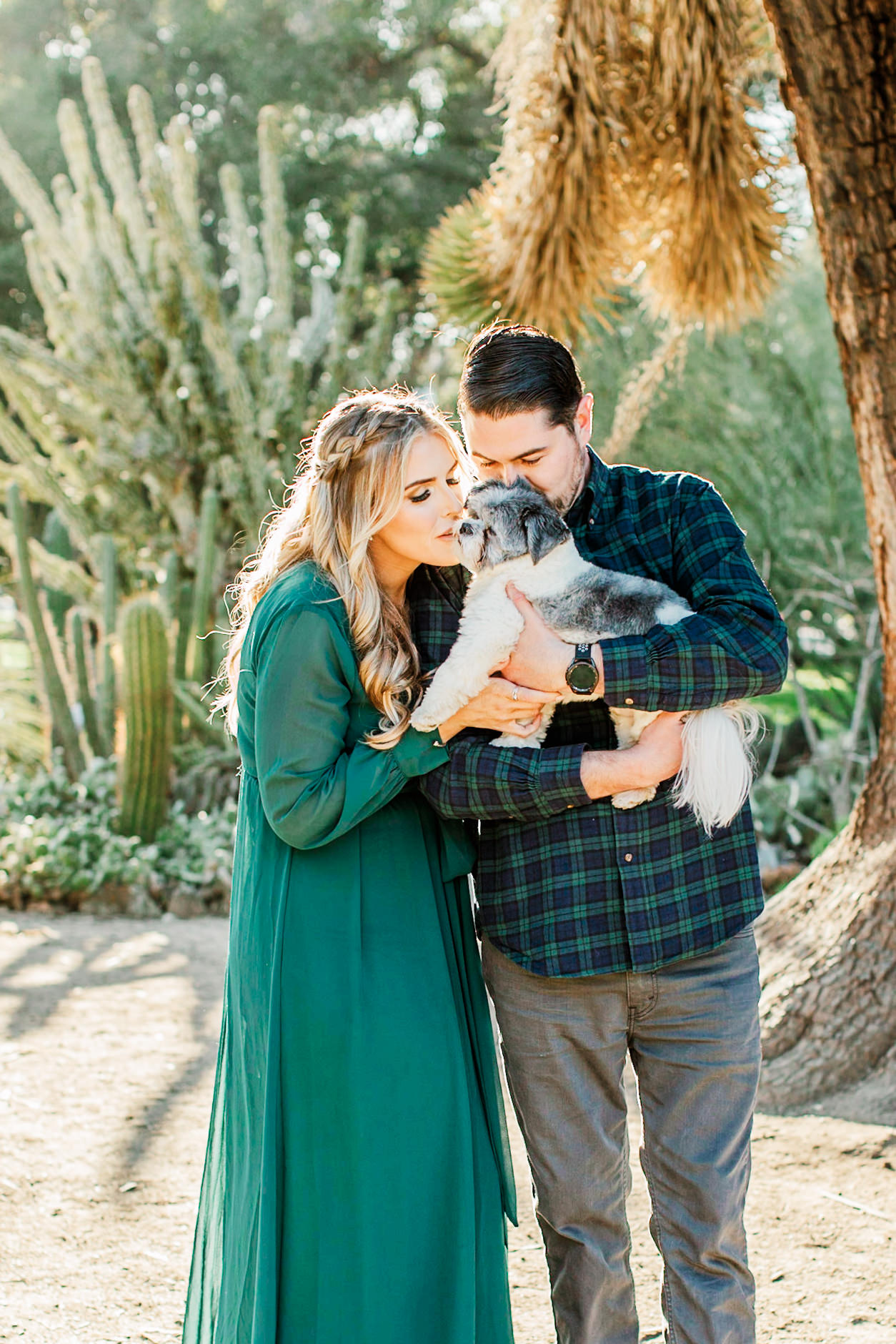 Engaged couple kissing their dog in golden light