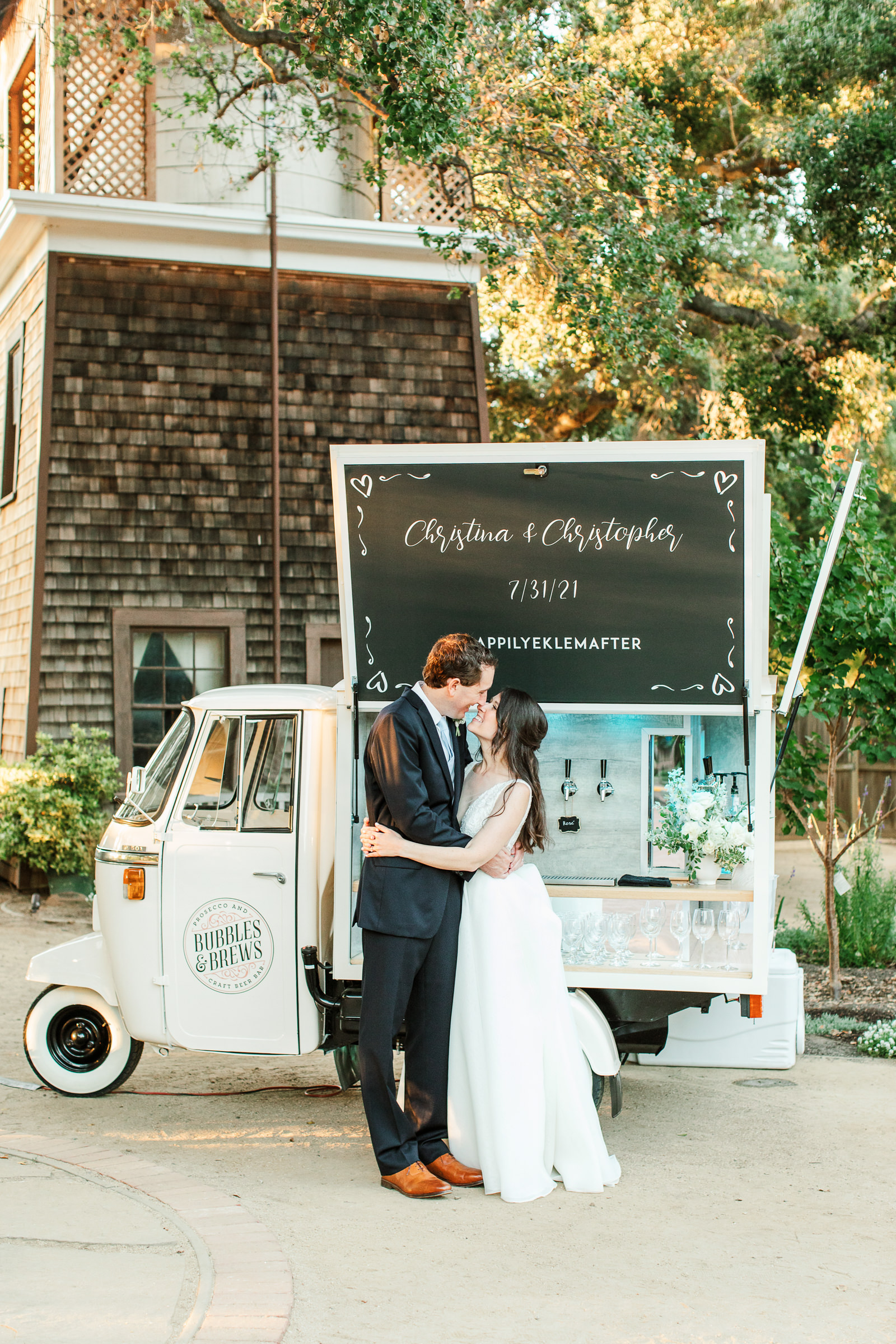 Bride and Groom hugging in the gardens of the Los Altos History Museum in front of a champagne cart during their wedding