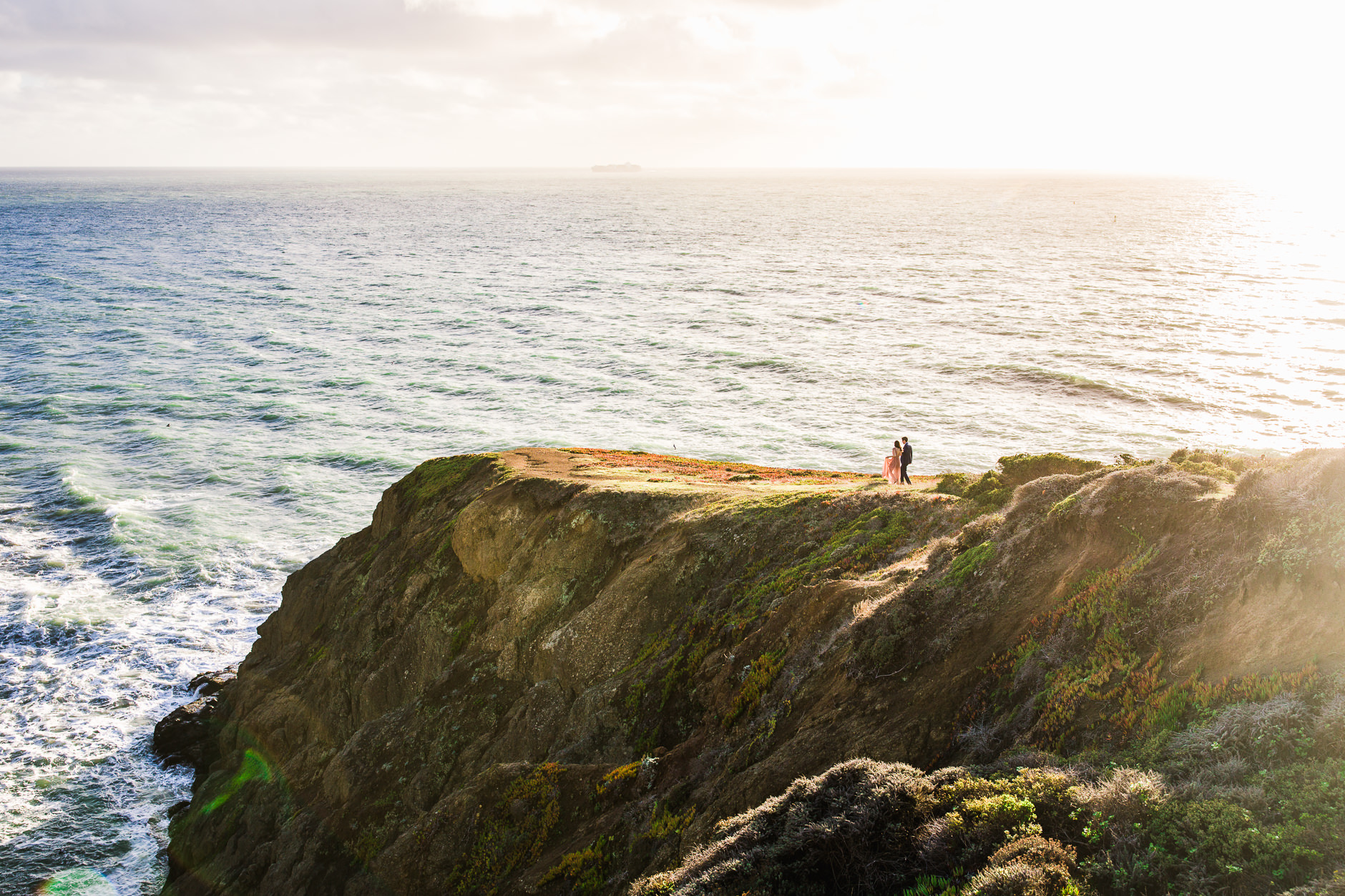 couple in long pink maxi dress and blue suit walking on marin headlands engagement photos