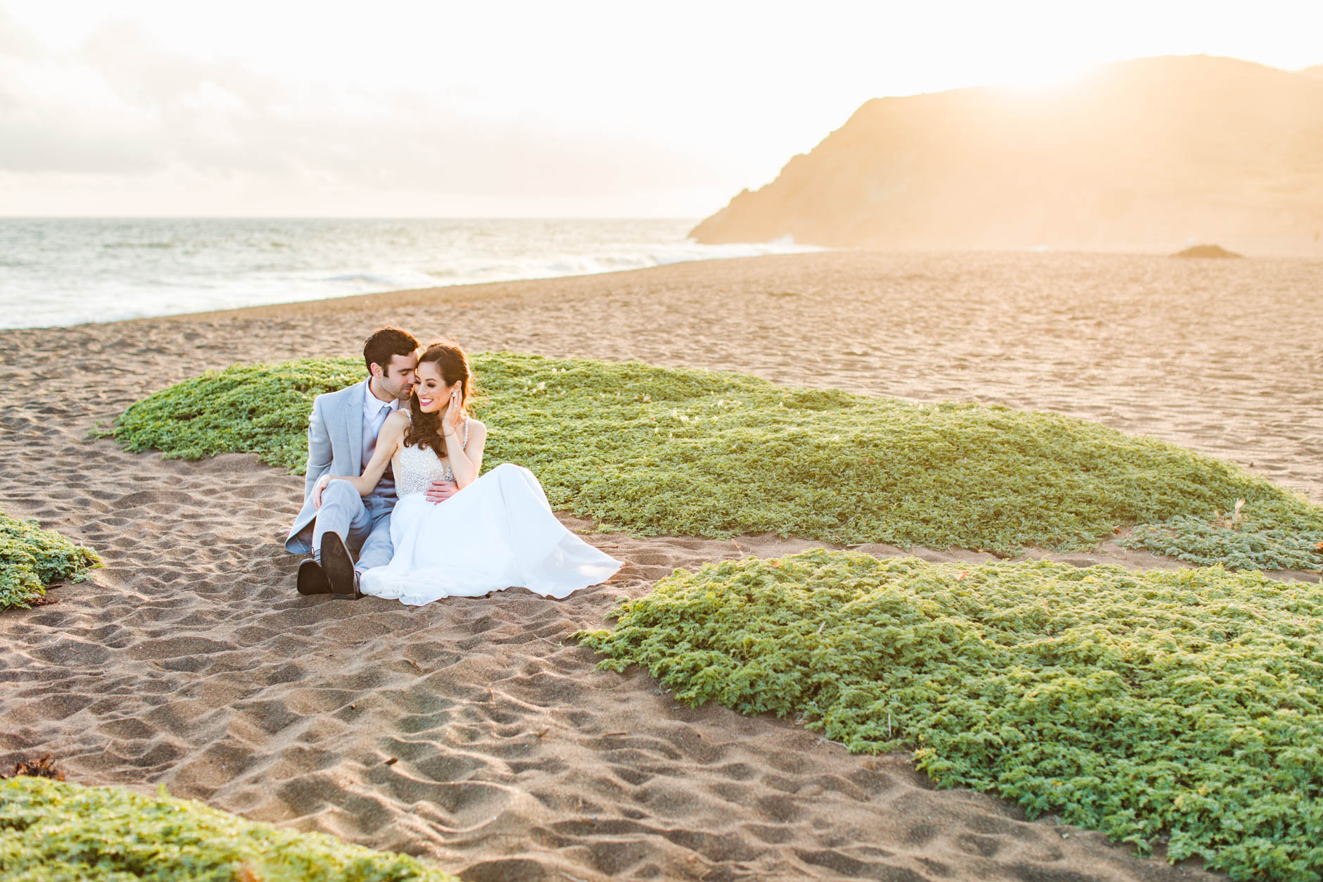 Bride and groom sitting on beach at sunset during windswept elopement