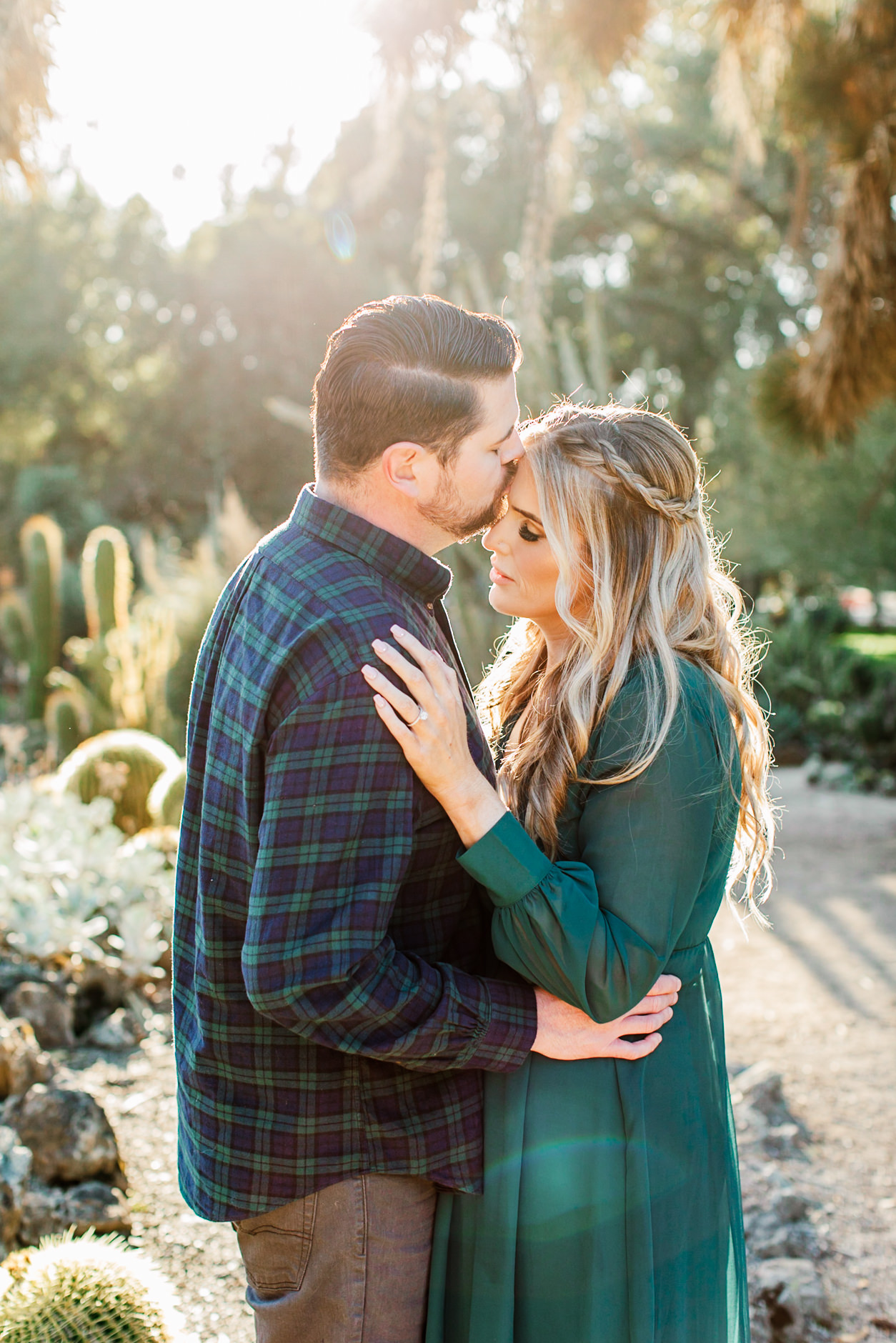 Man kissing his fiance on the forehead during their engagement session in golden backlight at the Arizona Cactus Garden